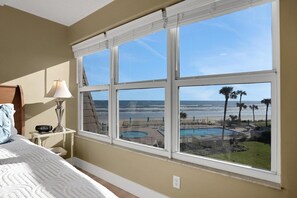 A bedroom with a large window overlooking a pool and beach. - Ocean front condo w/ gorgeous direct beach view & pool/tennis access! (St. Augustine)