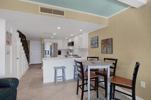 Una cocina moderna con armarios blancos, una isla central y un comedor con sillas de madera.