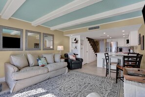 A living room with a sofa, a coffee table, and a patterned rug. There is a kitchen area with a refrigerator, a stove, and a sink. - Ocean front condo w/ gorgeous direct beach view & pool/tennis access! (St. Augustine)
