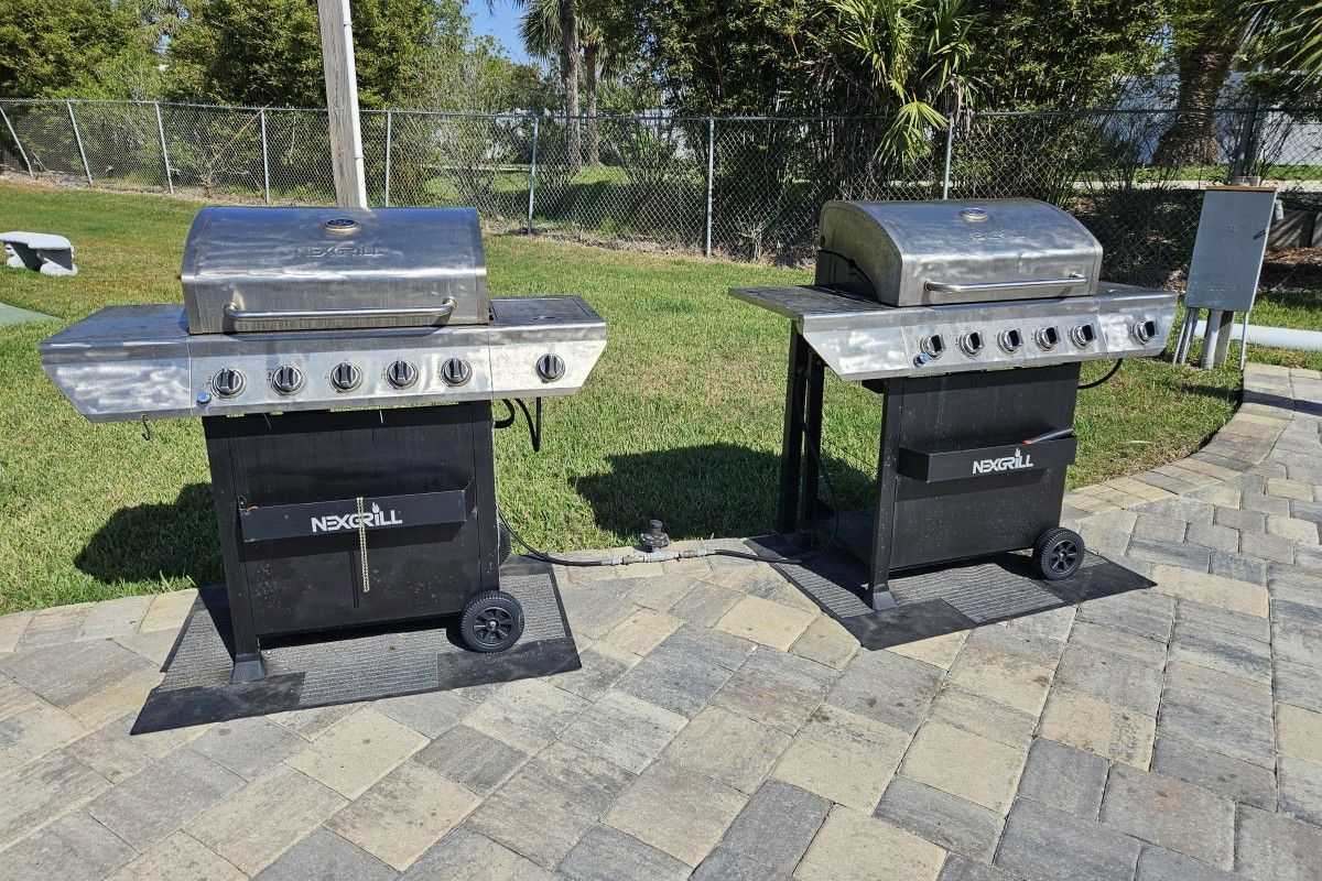 Deux barbecues à gaz portables, portant l’inscription « NEXGRILL », sont placés sur une terrasse dallée, avec une zone herbeuse et une clôture en arrière-plan.