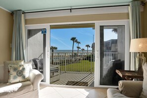 A room with a sliding glass door leading to a deck with a view of the ocean and palm trees. - Ocean front condo w/ gorgeous direct beach view & pool/tennis access! (St. Augustine)