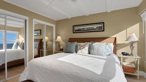 A bedroom with a large bed, a mirror, a nightstand, and a window with a view.