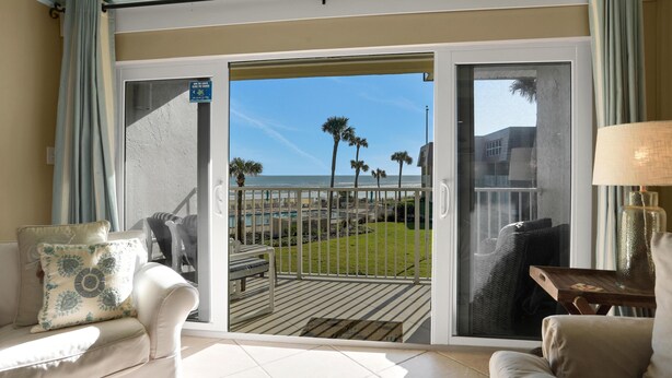Ein Zimmer mit einer Schiebeglasdoor zum Deck mit Blick auf den Ozean und Palmen.