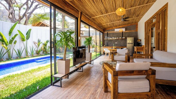 A modern living room with a wooden floor, large windows, and a pool view. - Casa Heaven Santa Teresa (Cóbano)