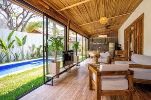 A modern living room with a wooden floor, large windows, and a pool view. - Casa Heaven Santa Teresa  (Cóbano)
