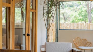 A modern interior with a glass-top table, wooden furniture, and a large window offering a view of greenery. - Casa Heaven Santa Teresa (Cóbano)