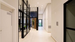A modern hallway with glass partitions, a visible door labeled "LAVANDERIA," and a plant in the background. - My One Bela Vista  (São Paulo)