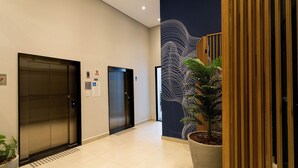 A modern elevator area with two elevators, a potted plant, and a decorative wall with a wave pattern. - My One Bela Vista  (São Paulo)