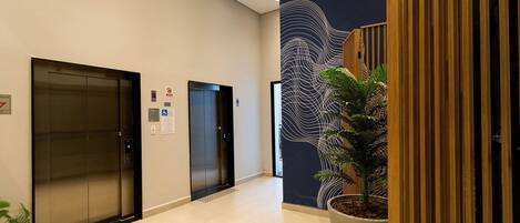 A modern elevator area with two elevators, a potted plant, and a decorative wall with a wave pattern.