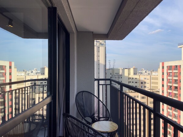 A balcony with a chair and a table, overlooking a cityscape with multiple buildings. - My One Bela Vista (São Paulo)
