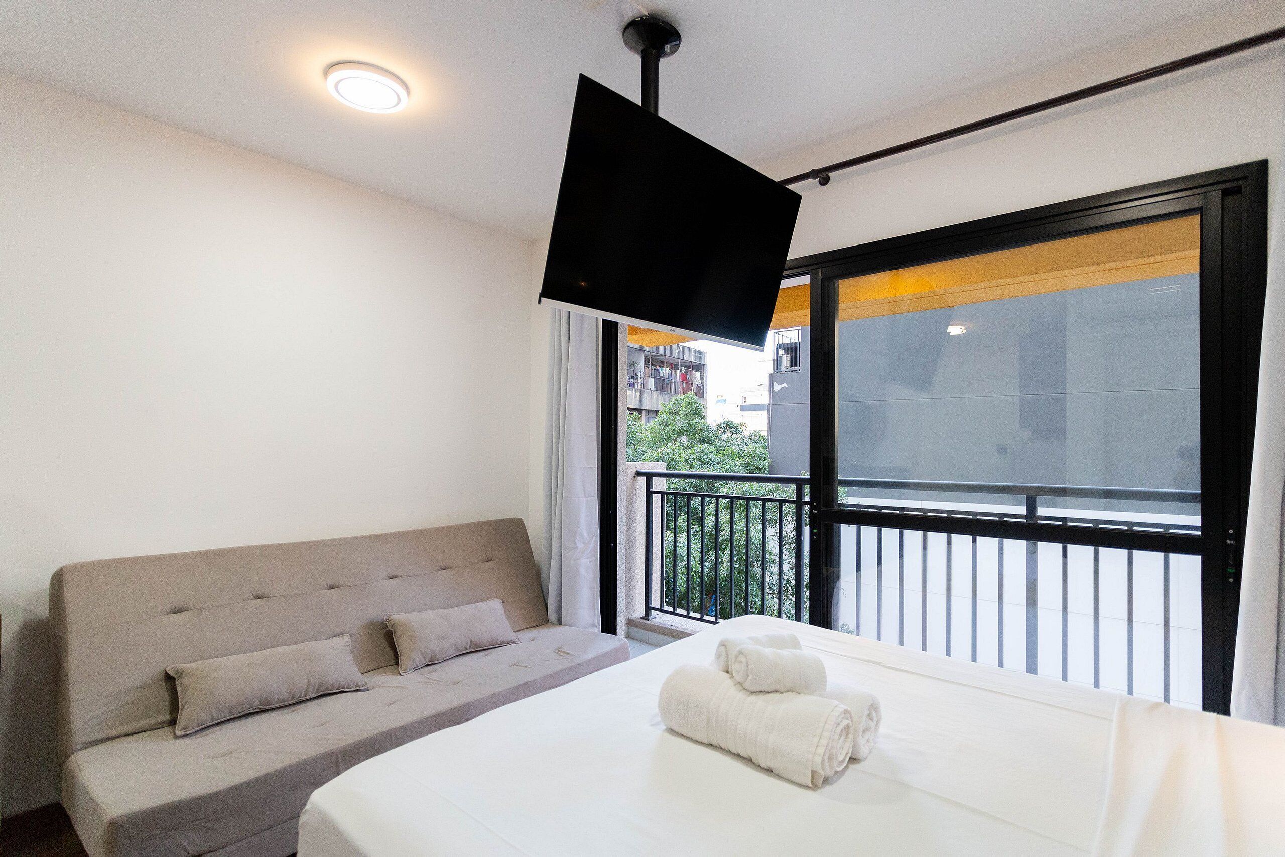 Een moderne hotelkamer met een bed, een slaapbank, een flatscreen-tv aan de muur en een balkon met uitzicht op de stad.