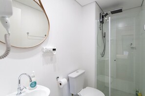 A bathroom with a sink, mirror, toilet, and glass-enclosed shower. - My One Bela Vista (São Paulo)