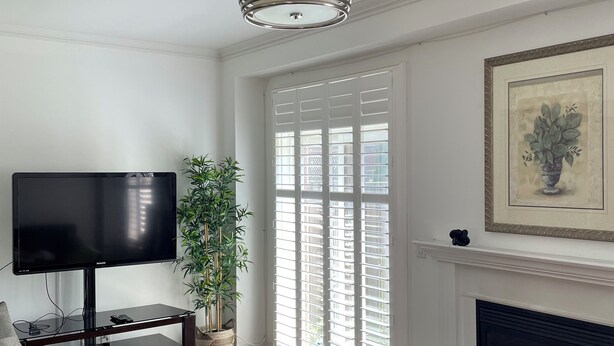 A living room with a flat-screen TV, a tufted ottoman, a potted plant, a fireplace, and a framed artwork. - Executive End Unit Townhome (Milton)