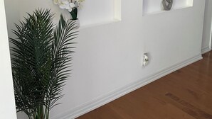 A hallway with white walls, two framed artworks, a potted plant, and a door with a white handle. - Executive End Unit Townhome (Milton)