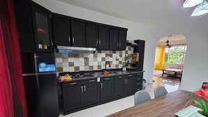 A modern kitchen with black cabinets, a stainless steel refrigerator, and a dining area with a wooden table.