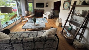 A cozy living room with a fireplace, a television, and a large window with curtains. - Robin's Bluff- Classic 3-bedroom in beautiful Whitefish Bay, convenient location (Whitefish Bay)