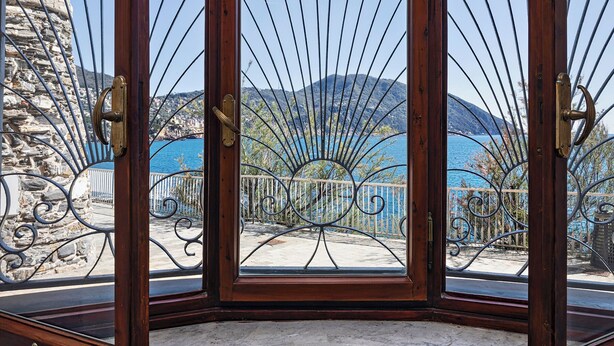 A wooden-framed window with a metal decorative grill, offering a view of a coastal town and a mountain range. - A Few Steps from the Sea by Wonderful Italy (Recco)