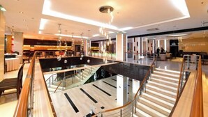 Eine moderne Hotelhalle mit großzügiger Sitzecke, einer Treppe und einem Glasgeländer.