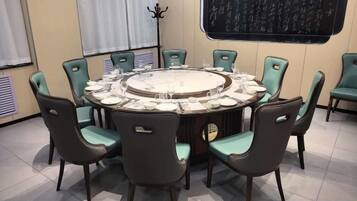 A round dining table with chairs, a blackboard on the wall, and a window with curtains.