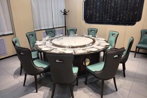 Une table de salle à manger ronde, entourée de chaises, un tableau noir accroché au mur et une fenêtre avec des rideaux.