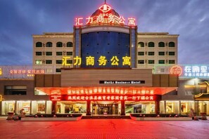 A hotel with a prominent sign, a large entrance, and a well-lit facade. - Huili Business Apartment (Jiayuguan Donghu Scenic Area Datang Food Street Branch) (Jiayuguan)