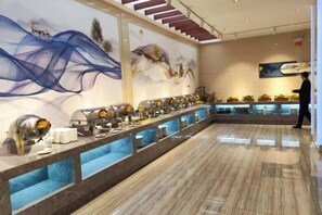 Un área de bufé con una barra larga, distintas estaciones de comida y un mural en la pared.