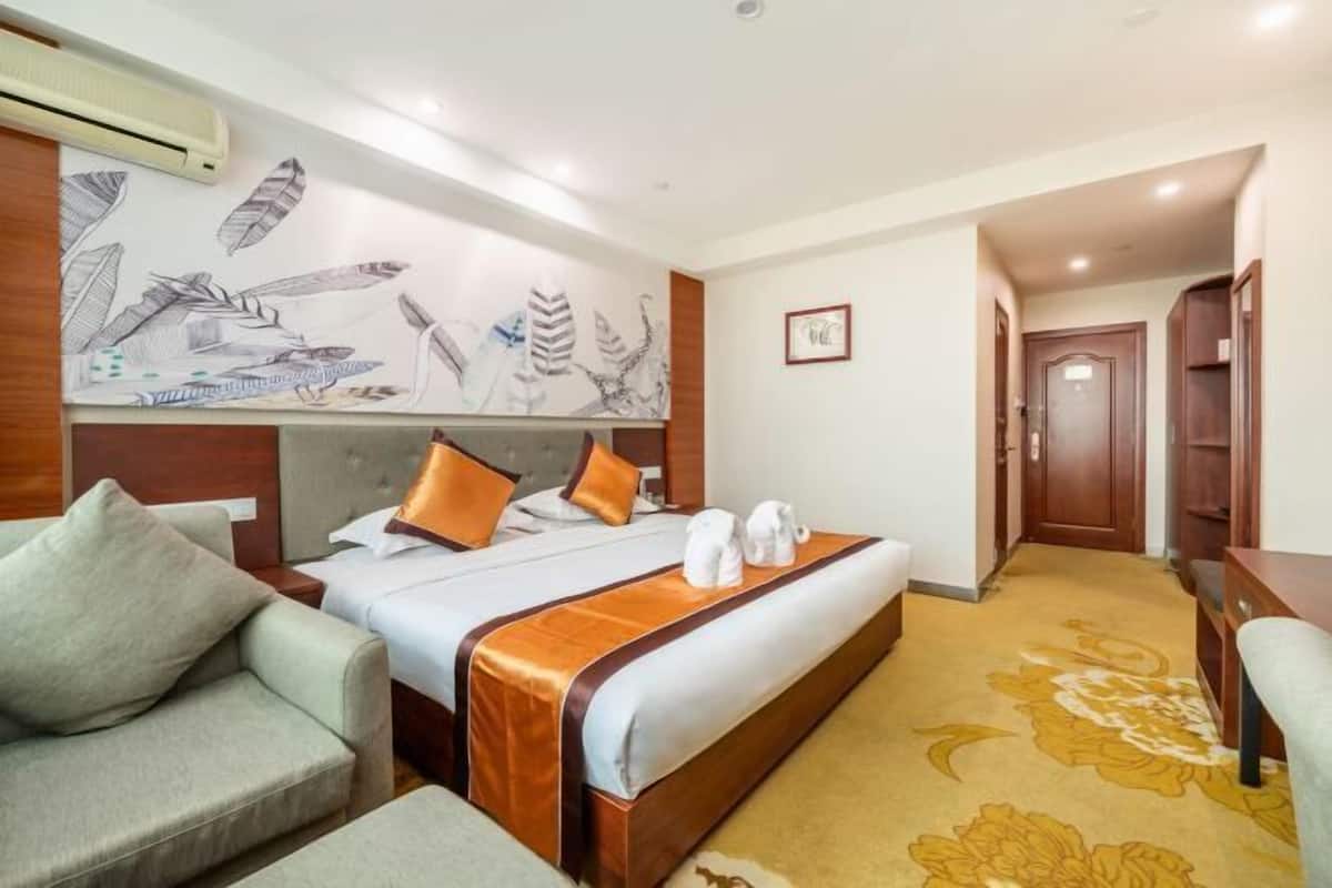 Une chambre d’hôtel comprenant un lit, deux oreillers, une tête de lit, une table de chevet, un canapé, une moquette et un mur orné d’une fresque.