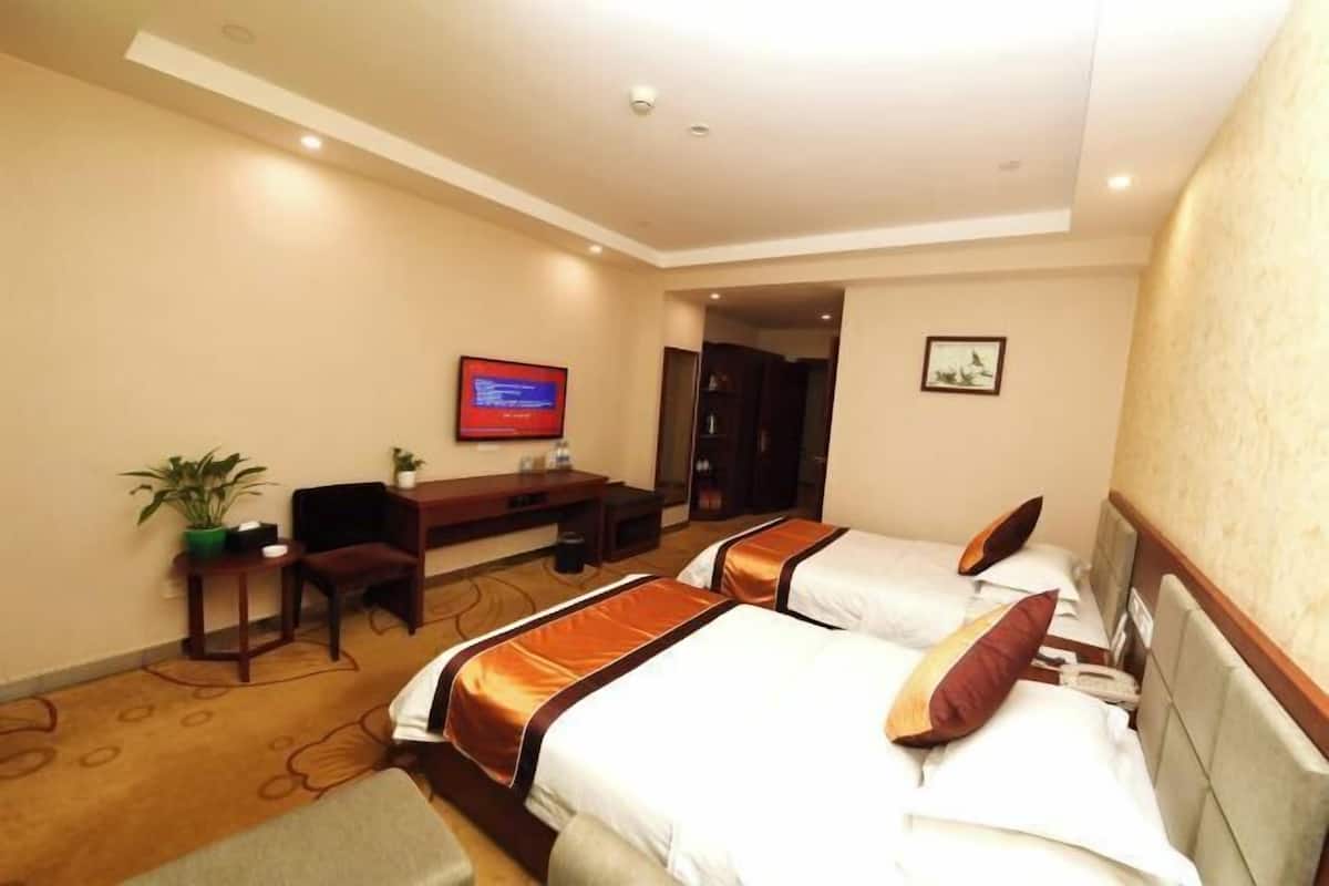 Une chambre d’hôtel avec trois lits, un bureau, une télévision et une petite plante.