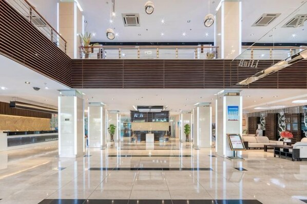 A spacious lobby with a reception desk, a staircase, and a second-floor balcony.