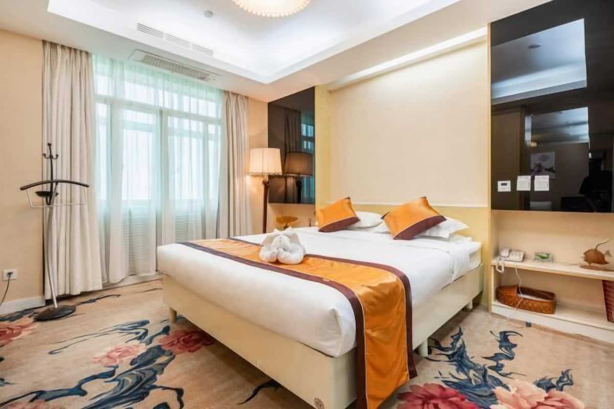 Une chambre d’hôtel avec un lit, une lampe de chevet, un miroir, un bureau et une fenêtre avec des rideaux.