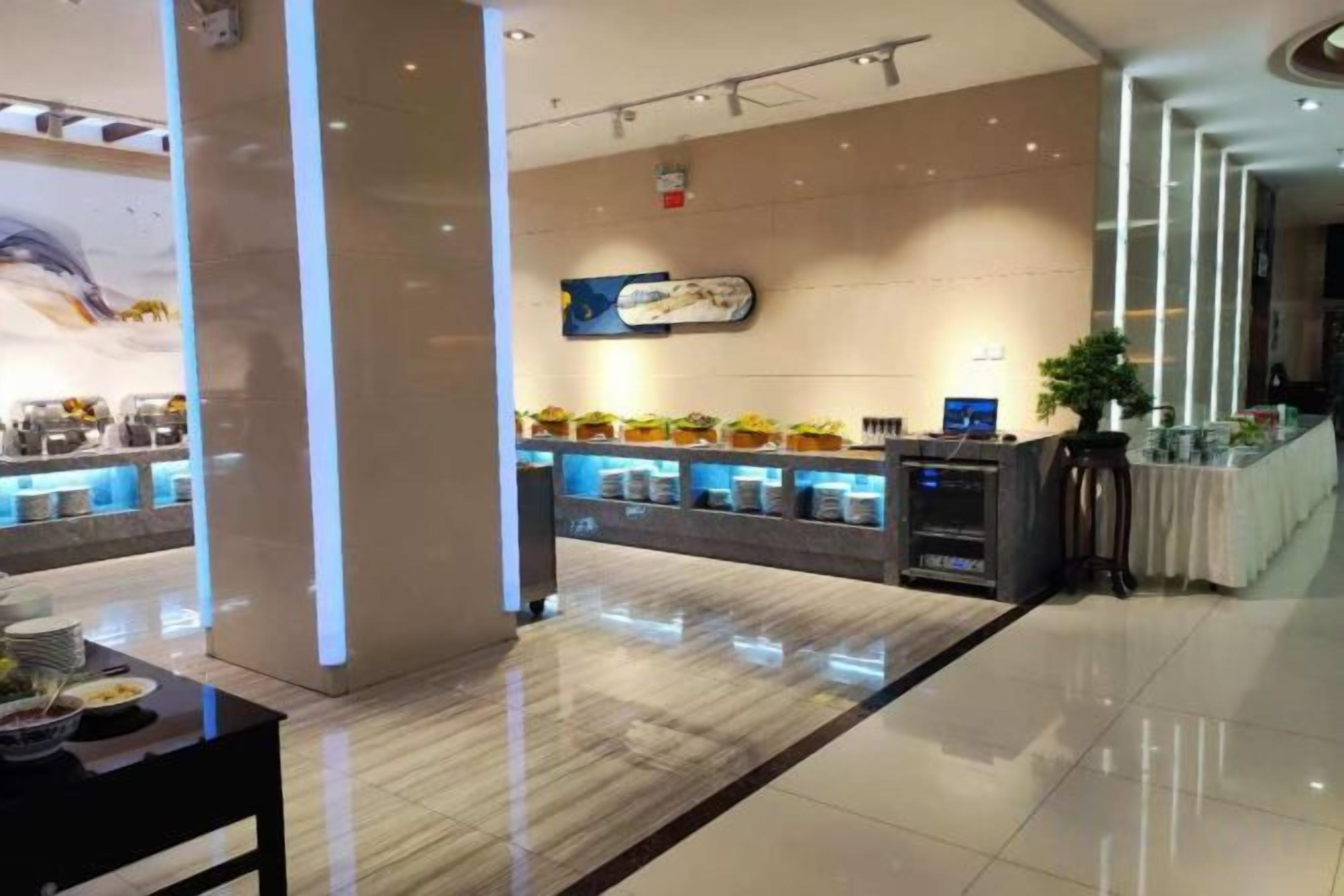 Un moderno vestíbulo de hotel con un mostrador de recepción, una zona de estar y una barra con productos alimenticios.