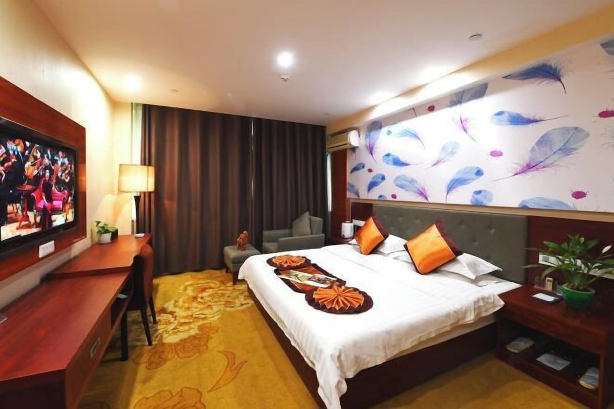 Habitación de hotel con cama, escritorio, televisor, pared con diseño de plumas y planta.