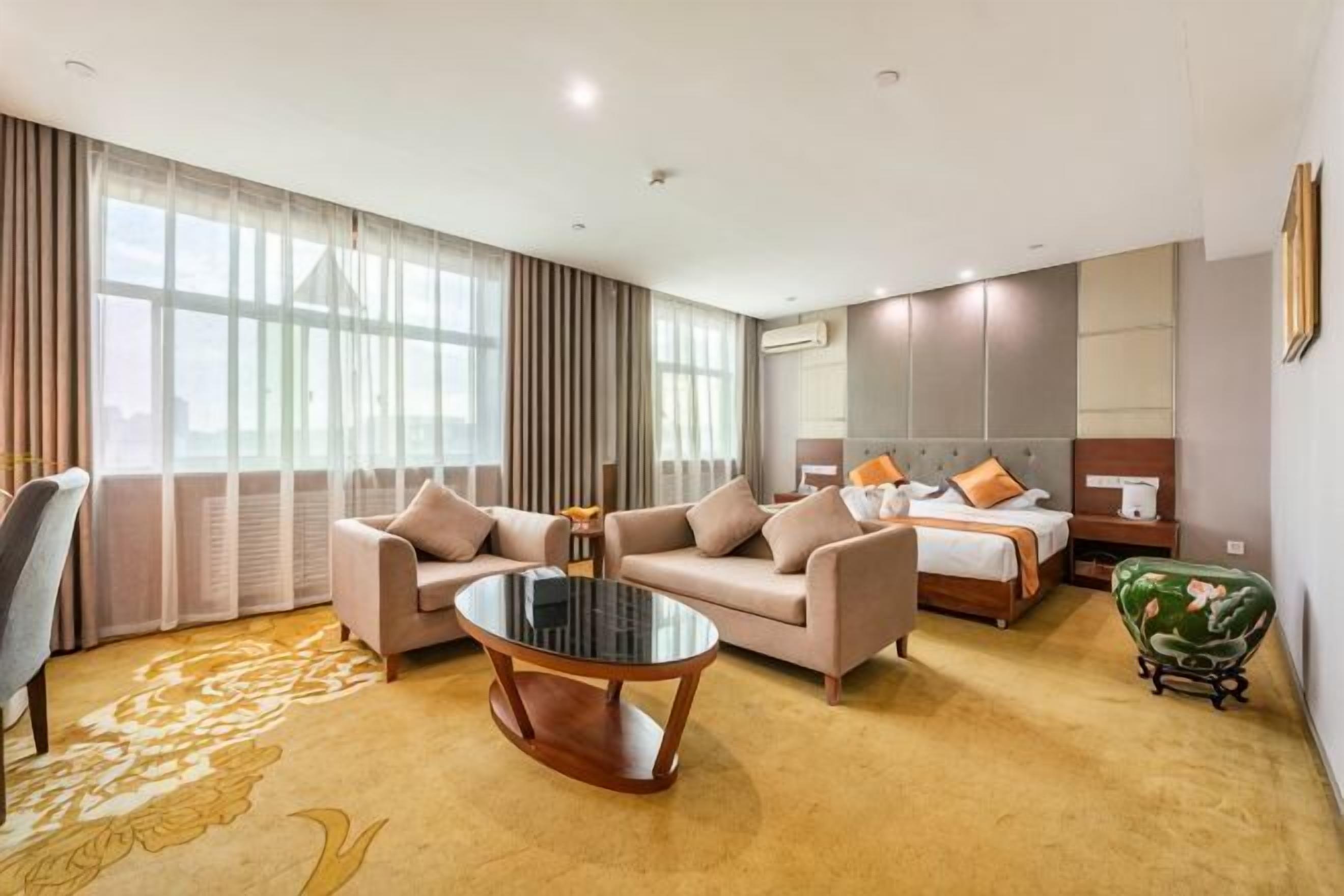 Una habitación de hotel con sofá, una mesita redonda, una cama con almohadas, una mesita de noche y un sillón verde.