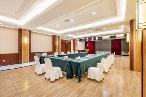 Un salón de conferencias con una larga mesa, sillas blancas y un escenario con una cortina roja.