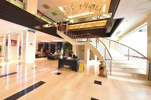 Un vestíbulo amplio con una escalera central, un mostrador de recepción y un área de estar.