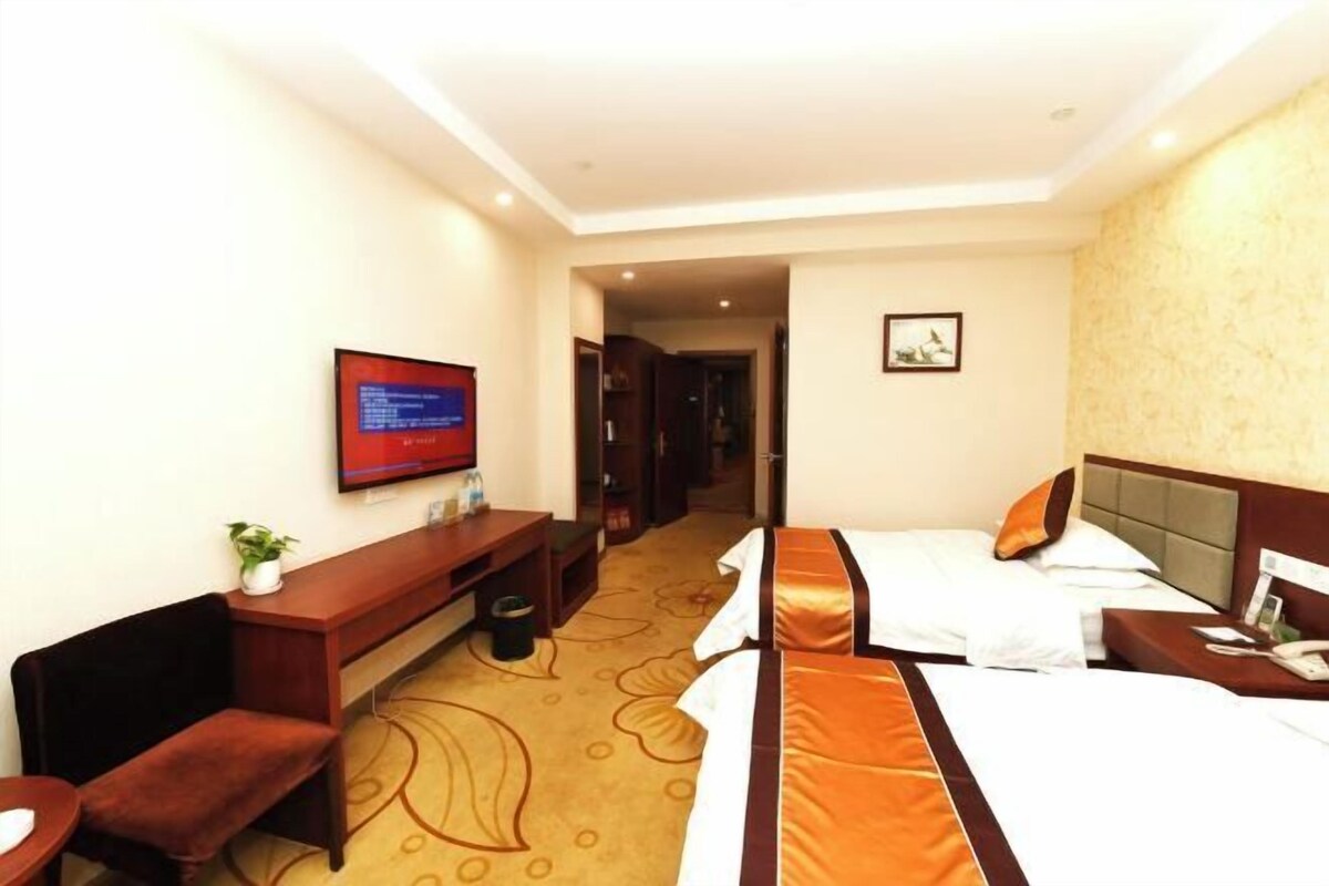 Habitación de hotel con cama, escritorio, silla, televisor y puerta que da a otra habitación.