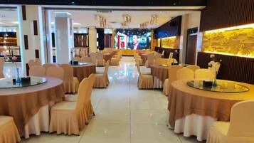 Une salle à manger d’hôtel avec des tables et des chaises rondes, une scène centrale et un mur décoratif.