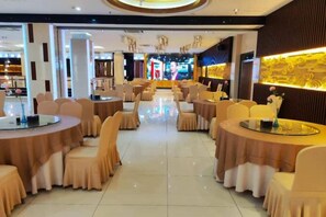A hotel dining area with round tables and chairs, a central stage, and a decorative wall. - Huili Business Apartment (Jiayuguan Donghu Scenic Area Datang Food Street Branch) (Jiayuguan)