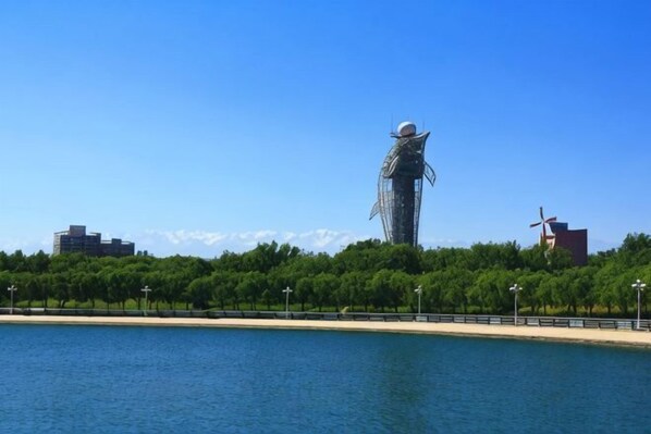 A large sculpture by the water with a clear view of the surrounding park and distant buildings. - Huili Business Apartment (Jiayuguan Donghu Scenic Area Datang Food Street Branch) (Jiayuguan)