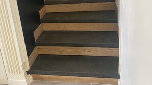 Una escalera de madera con peldaños y largueros oscuros, que lleva a una puerta.