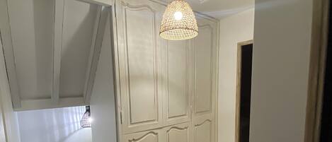 A hallway with a wooden floor, a white door, and a hanging light fixture.