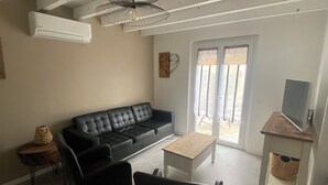 Una sala de estar con un sofá de cuero negro, dos sillas negras, una mesa de centro de madera, un televisor sobre un mueble de madera y un ventilador de techo.
