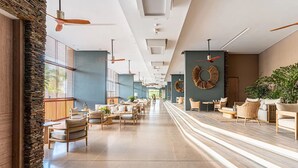 Un hall d’hôtel spacieux, doté d’un long comptoir d’accueil, de plusieurs espaces salon et d’un design moderne au niveau du plafond.