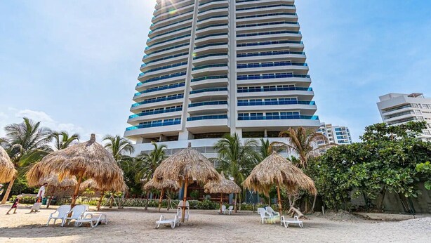 Un grand hôtel doté de nombreux balcons, entouré de parasols en chaume et de chaises de plage.