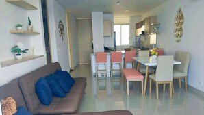 Un salon moderne avec un canapé marron, un coin repas avec des chaises roses et une cuisine en arrière-plan.