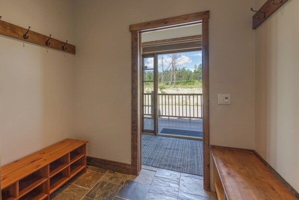 A room with a wooden bench, a stone-tiled floor, a wooden door leading to a balcony, and a metal railing. - Spacious | Hot Tub | Pet-Friendly | Mountain Views | Fire Pit | Golf
(Invermere)