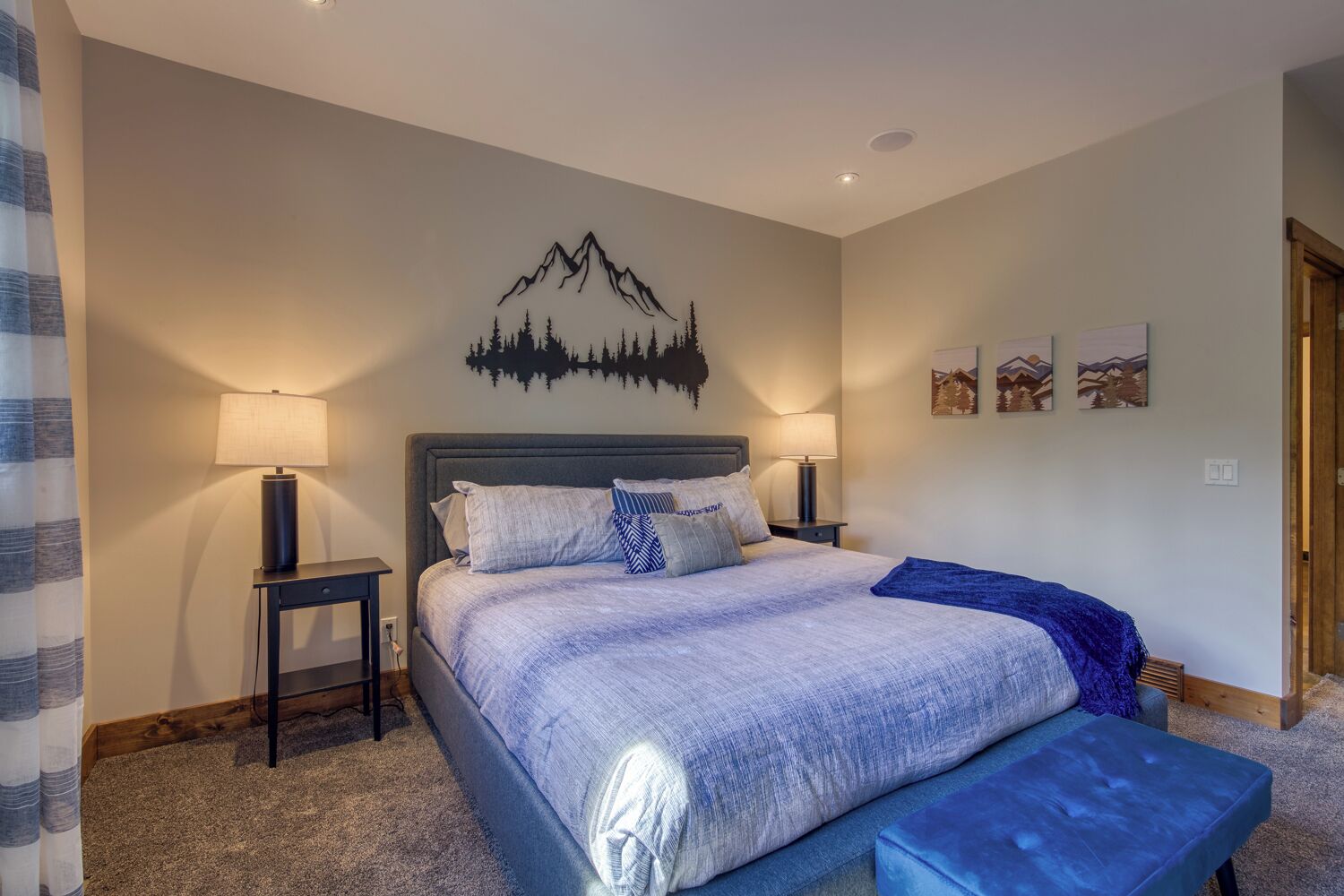 A bedroom with a bed, two bedside tables, a headboard, a wall-mounted artwork of a mountain, and a door.