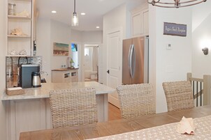 A kitchen with a stainless steel refrigerator, a coffee maker, and a wicker chair.