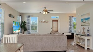 A living room with a sofa, television, ceiling fan, and decorative items. - Pixie's Paradise (Port St. Joe)