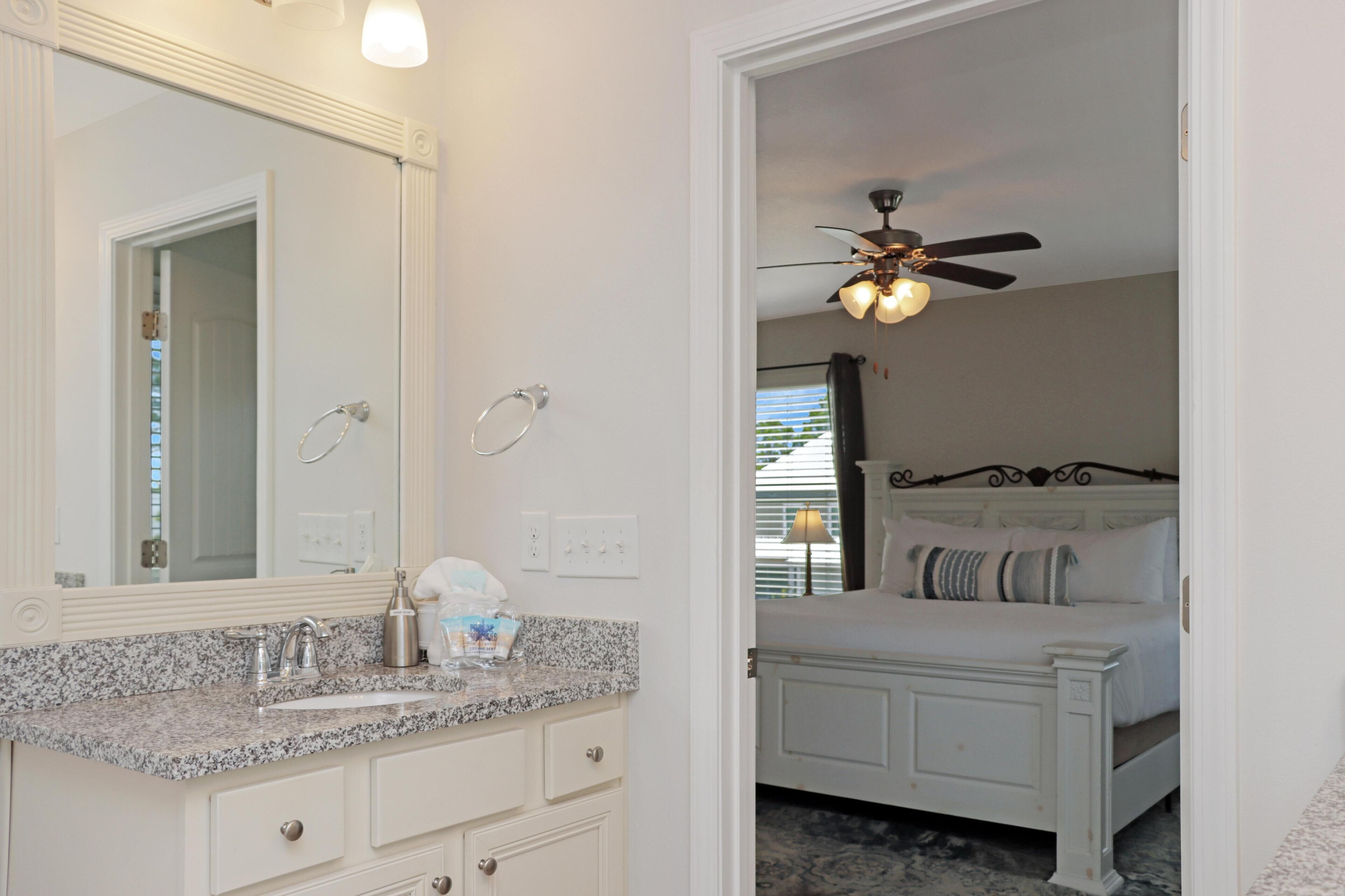 A bathroom with a granite countertop, a large mirror, and a ceiling fan.